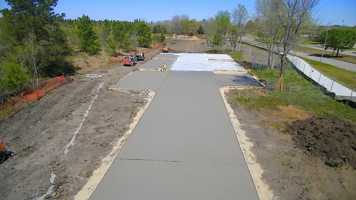 Aerial view of a long concrete driveway pour framed by trees.